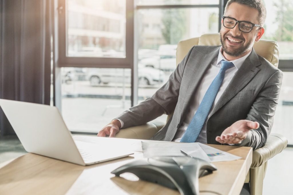 A imagem mostra um homem de negócios sentado em uma mesa, com um notebook na sua frente. Foto para ilustrar o texto sobre corretor de imóveis de alta performance