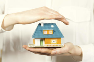 A imagem mostra duas mãos segurando a maquete de uma casa, como forma de proteção. Foto para ilustrar o texto sobre seguro fiança