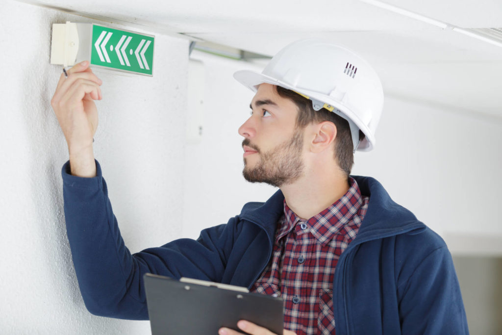 A imagem mostra um homem verificando um item de sinalização de um prédio. Foto para ilustrar o texto sobre manutenção preventiva