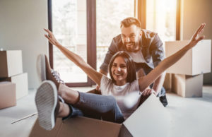 A imagem mostra um casal se divertindo dentro de uma casa. Foto para ilustrar o artigo sobre comprar ou alugar imóvel