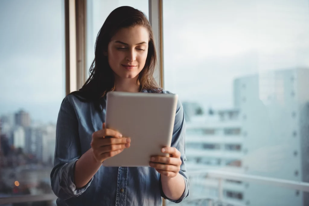 A imagem mostra uma mulher, dentro de uma sala comercial em um prédio, segurando um tablet. Foto para ilustrar o texto sobre processo de locação de imóvel