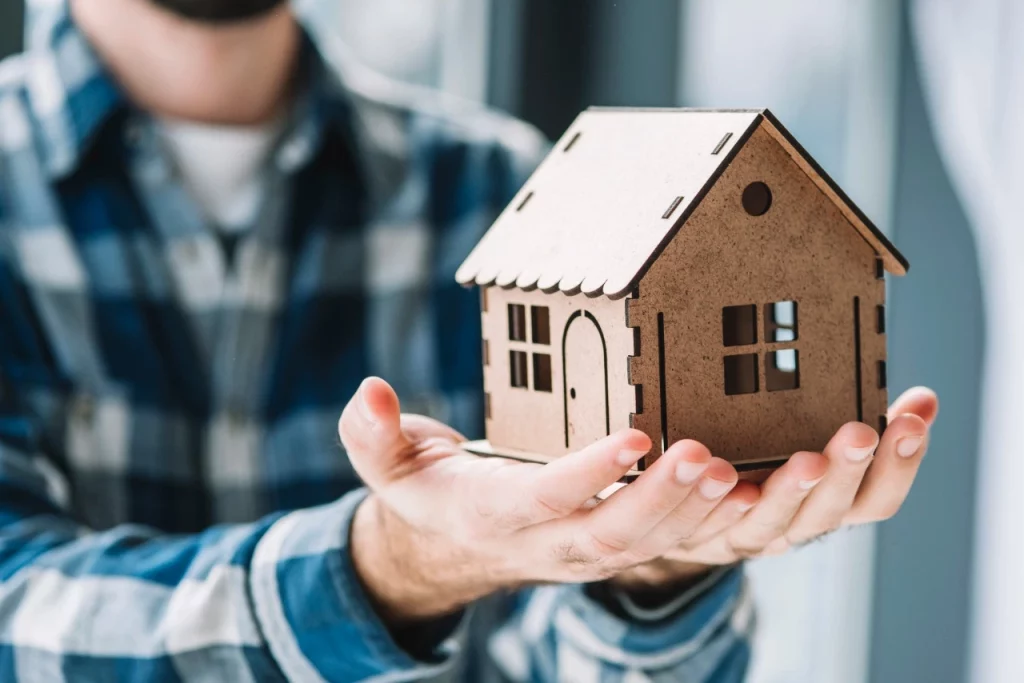 A imagem mostra uma pessoa mostrando o modelo de uma casa. Foto para ilustrar o texto sobre seguro incêndio