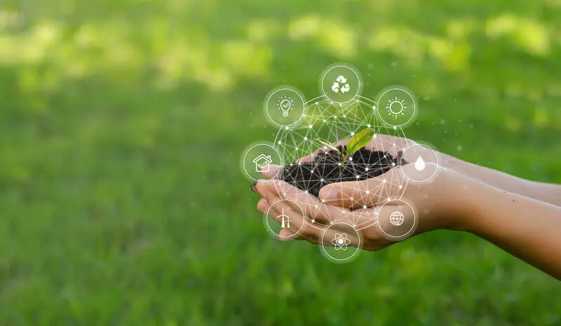 A foto mostra uma mão com terra e uma planta. Ao redor dela temos os conceitos de ESG conectados entre si, formando a imagem de um globo